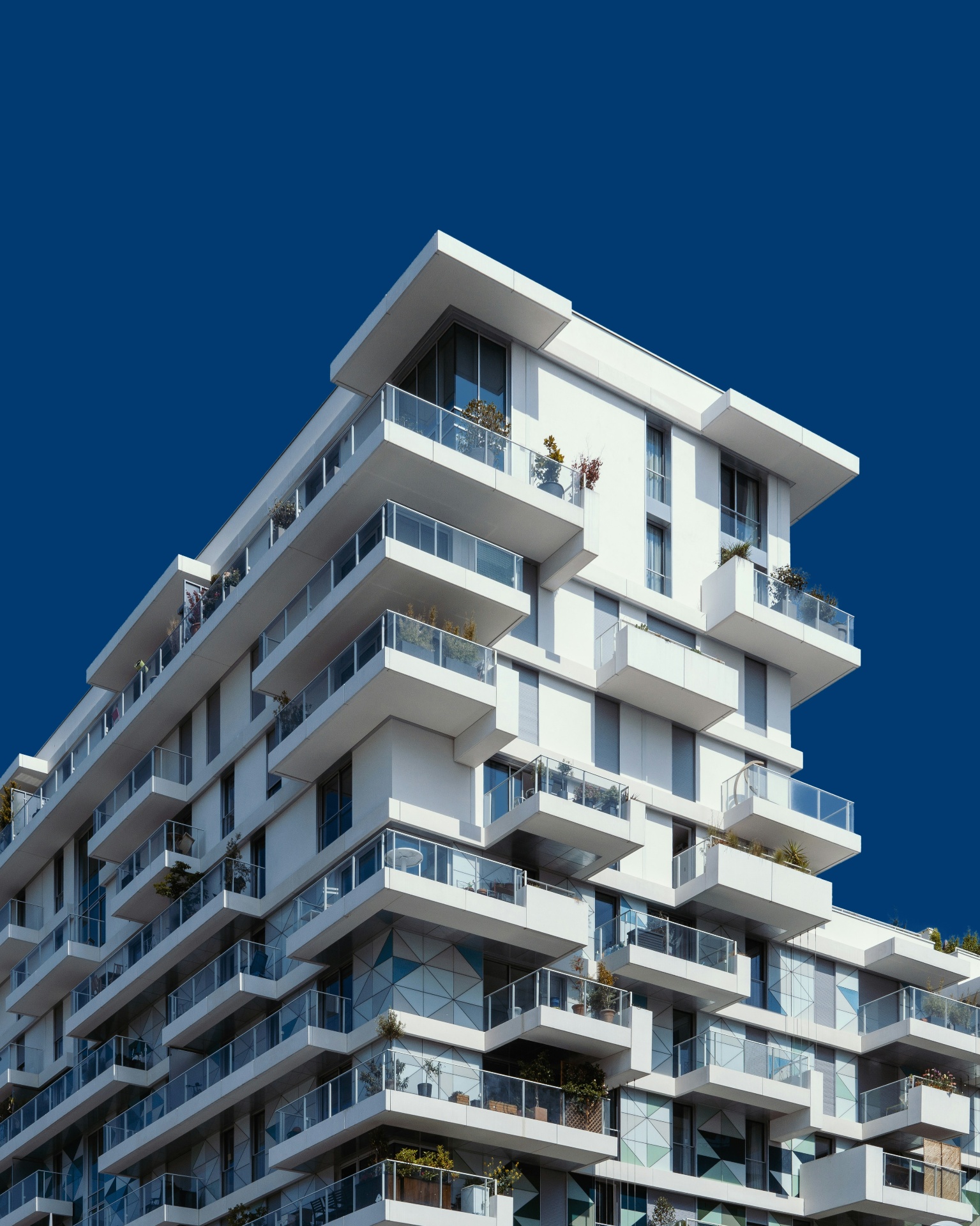 Modern white residential tower with cascading balconies against a deep blue sky